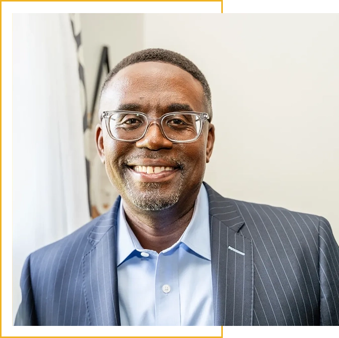 A man in a suit and glasses smiling for the camera.